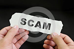 Scammed victim concept. Hand holding a piece of paper with word scam in dark black background.