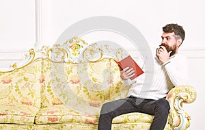 Scandalous bestseller concept. Guy reading book with amazement. Man with beard and mustache sits on baroque style sofa