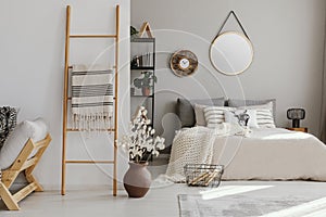 Scandi open space bedroom interior with bed with knit blanket and many pillows, rack with books and decor, carpet on the