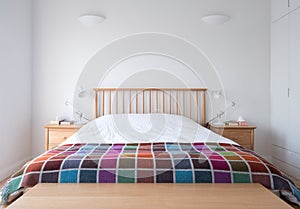 Scandi style bedroom interior with wooden bedroom furniture, white painted walls, white bedding and colourful blanket.