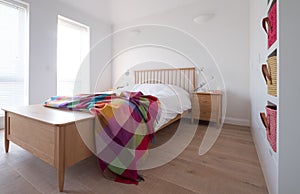 Scandi style bedroom interior with wooden bedroom furniture, white painted walls, white bedding and colourful blanket.