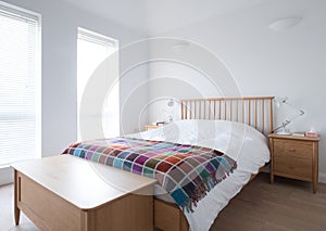 Scandi style bedroom interior with wooden bedroom furniture, white painted walls, white bedding and colourful blanket.