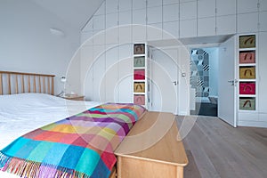 Scandi style bedroom interior with wooden bedroom furniture, white painted walls, white bedding and colourful blanket.