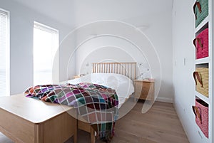 Scandi style bedroom interior with wooden bedroom furniture, white painted walls, white bedding and colourful blanket.