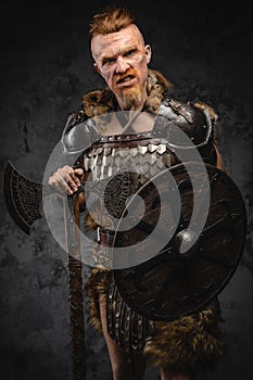 Scandinavian barbarian with shield and axe against dark background