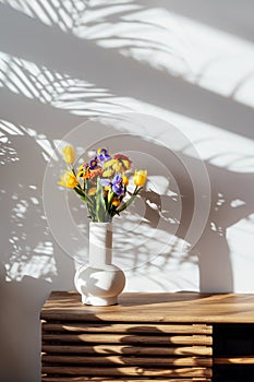 Scandinavian home interior with colorful bouquet of various flowers in ceramic vase standing on wooden cabinet under