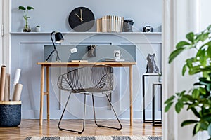 Scandinavian home office interior with wooden desk, design chair, wood panleing with shelf, plant, table lamp, office supplies.