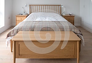 Scandinavian inspired, minimalist bedroom interior showing wooden bedroom furniture, white walls and bedding and woollen blanket