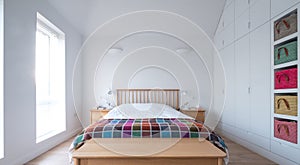 Scandi style bedroom interior with wooden bedroom furniture, white painted walls, white bedding and colourful blanket.