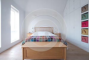 Scandi style bedroom interior with wooden bedroom furniture, white painted walls, white bedding and colourful blanket.