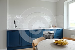 Scandinavian interior design. Blue kitchen cabinets, dining table with fruits. Nordic style room