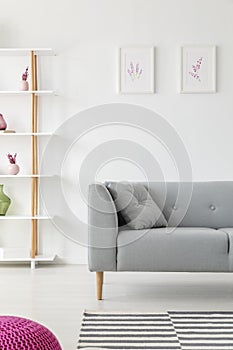 Scandinavian living room design with grey couch, heater prints on the wall and wooden shelf with vases on it