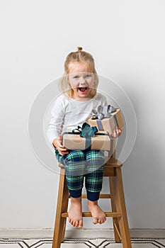Scandinavian minimalism christmas and new year concept with kid - little girl with stack of gift box on a chair in room