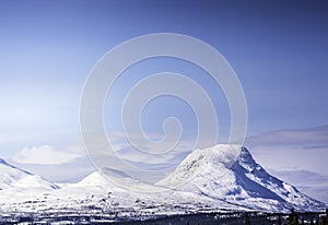 Scandinavian mountain range covered by ice and snow, blue skies, pine forest below the tops, Northern Norway