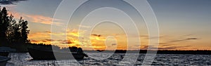 Scandinavian panorama of white night in Sweden. Motor boats at lake. Midnight Sun just below horizon line, golden sun rays