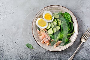 Scandinavian salad with smoked pink salmon, spinach, cucumber and chicken egg in gray ceramic dish.