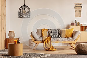 Scandinavian sofa with pillows and dark yellow blanket in bright living room interior with black chandelier