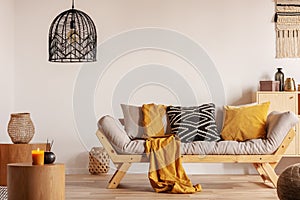 Scandinavian sofa with pillows and dark yellow blanket in bright living room interior with black chandelier
