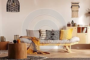 Scandinavian sofa with pillows and dark yellow blanket in bright living room interior with black chandelier