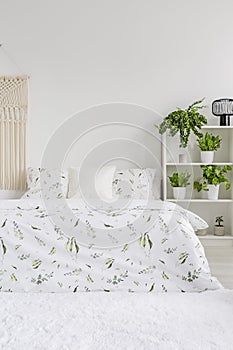 Scandinavian style bedroom interior with green plants pattern on white bedding lying on a bed. Fluffy rug on the floor. Empty wall