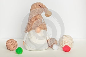 Scandinavian swedish gnome in white clothes and beige hat among woolen balls on a white background