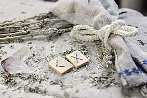 Scandinavian wooden rune Kenaz and Gebo on a rough linen cloth with amethyst crystalline, rock crystal and dried wormwood