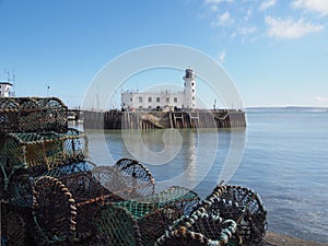 Scarborough lighthouse and harbour entrance reflected in a blue summer sea with stacked lobster pots