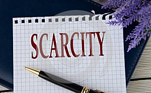 SCARCITY - word on a white sheet with a black notepad and pen