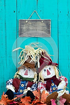 Scarecrows sitting under blank sign by fall foliage decor