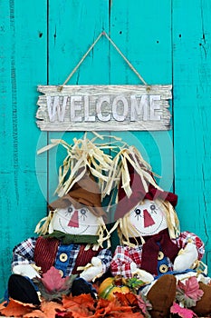Scarecrows sitting under welcome sign with fall decor