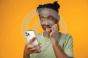 Scared african american woman holding mobile phone seeing bad news against yellow background