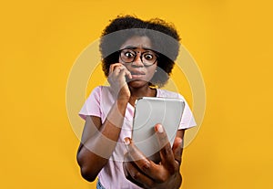 Scared african american woman holding mobile phone seeing bad news, photos or message over yellow background