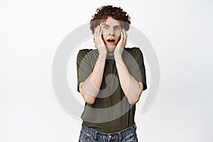 Scared and anxious curly guy freak out, screaming from fear and staring at camera shocked, standing over white