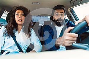 Scared arab couple looking at road with shocked expression, having risk of traffic accident driving car and braking hard