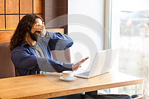 Scared bearded young man freelancer in casual style and long curly hair sitting and talking with his friend in laptop, covering