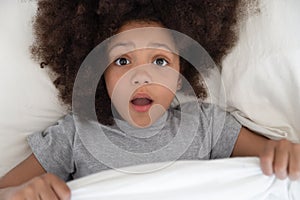 Scared biracial small girl peek from duvet having bad dream