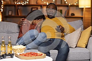 Scared black couple watching horror movie at home