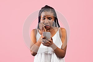 Scared black woman looking at smartphone in terror, seeing bad news, photos or message on pink background