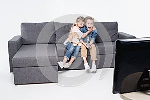 Scared boy and girl sitting on sofa and watching tv together