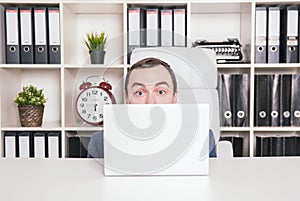 Scared business man hiding behind laptop