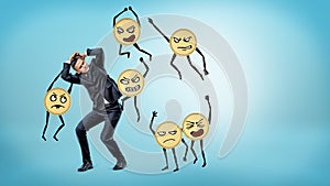 A scared businessman standing and hiding his face and body from many humanoid golden coins beating him.