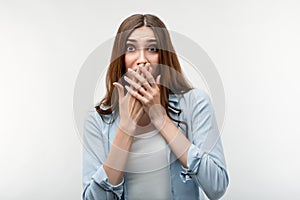 Scared caucasian girl with long chestnut hair covering mouth with hands on white background. Keep silence concept