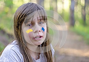 Scared child crying alone in the woods. Sign of Ukrainian flag on kid`s cheek. Ukrainian geopolitics globe crisis.