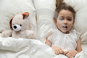 Scared child lying in bed with toy afraid of nightmare