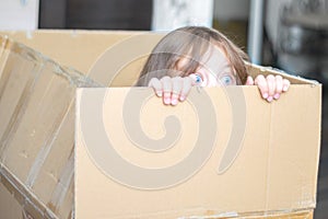 A scared child is sitting inside the mail box. A little girl peeks out of a square box. The baby hid from her parents