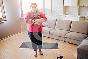 Scared confused young plus size model look on camera. Holding weight scale in hands. Stand in living room. Body positive