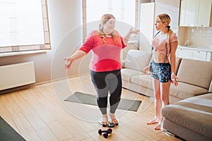 Scared confused young slim model look at plus size woman. Overweight girl stand on weight scale and smile. Jumping rope