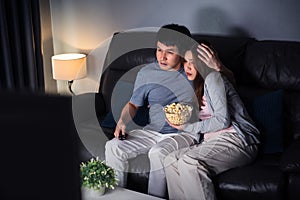 Scared couple is watching horror movie TV on sofa at night