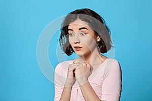 scared curly young brunette woman on blue background.