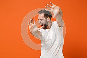 Scared displeased young man in casual white t-shirt posing isolated on orange background, studio portrait. People